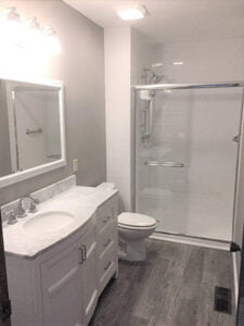 A bathroom remodel featuring a white vanity with a sink, a toilet, and a clear glass shower